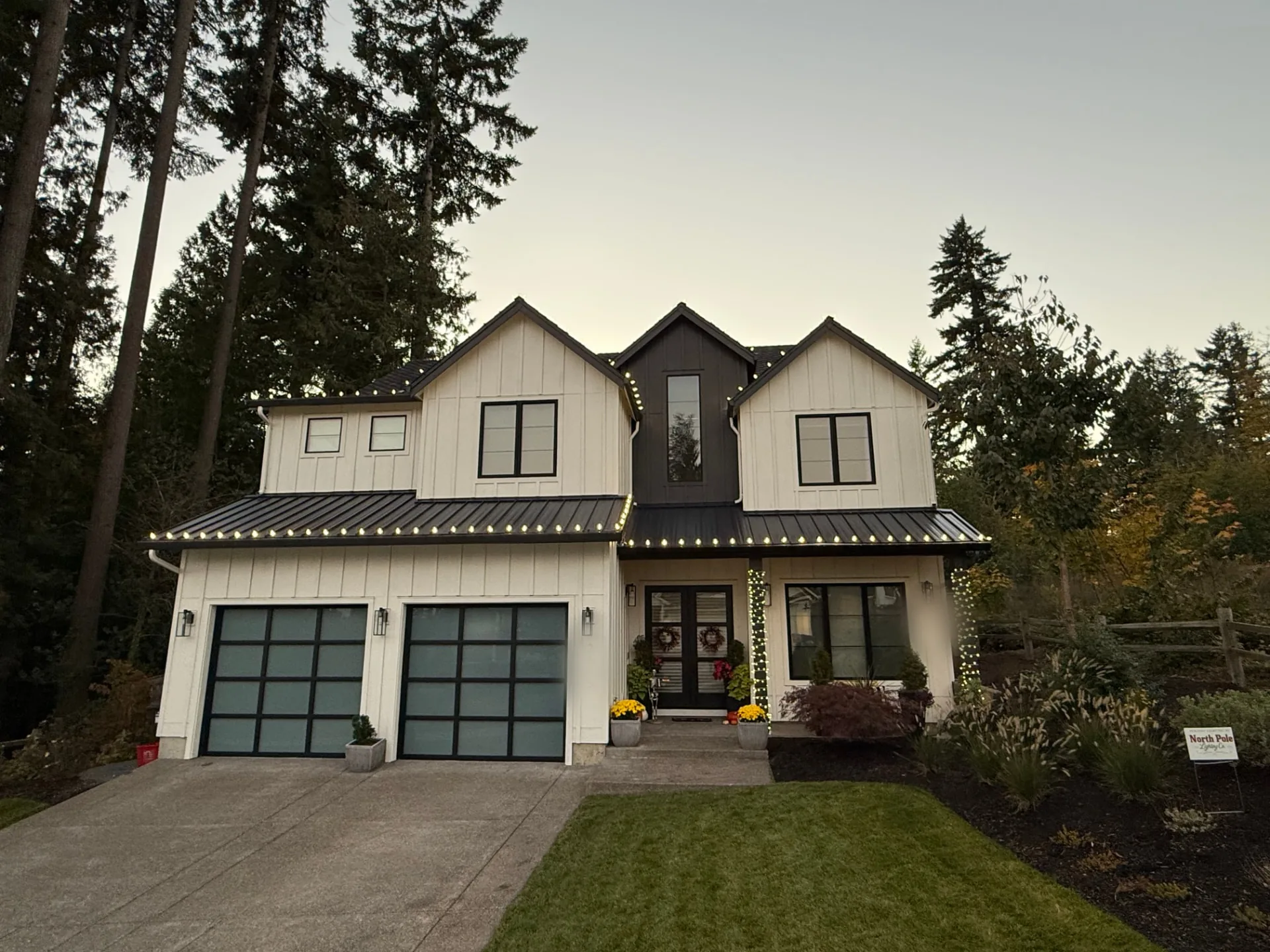 Modern farmhouse at dusk with warm white C9 bulbs along every roofline and gable and warm mini lights wrapped up the entry columns
